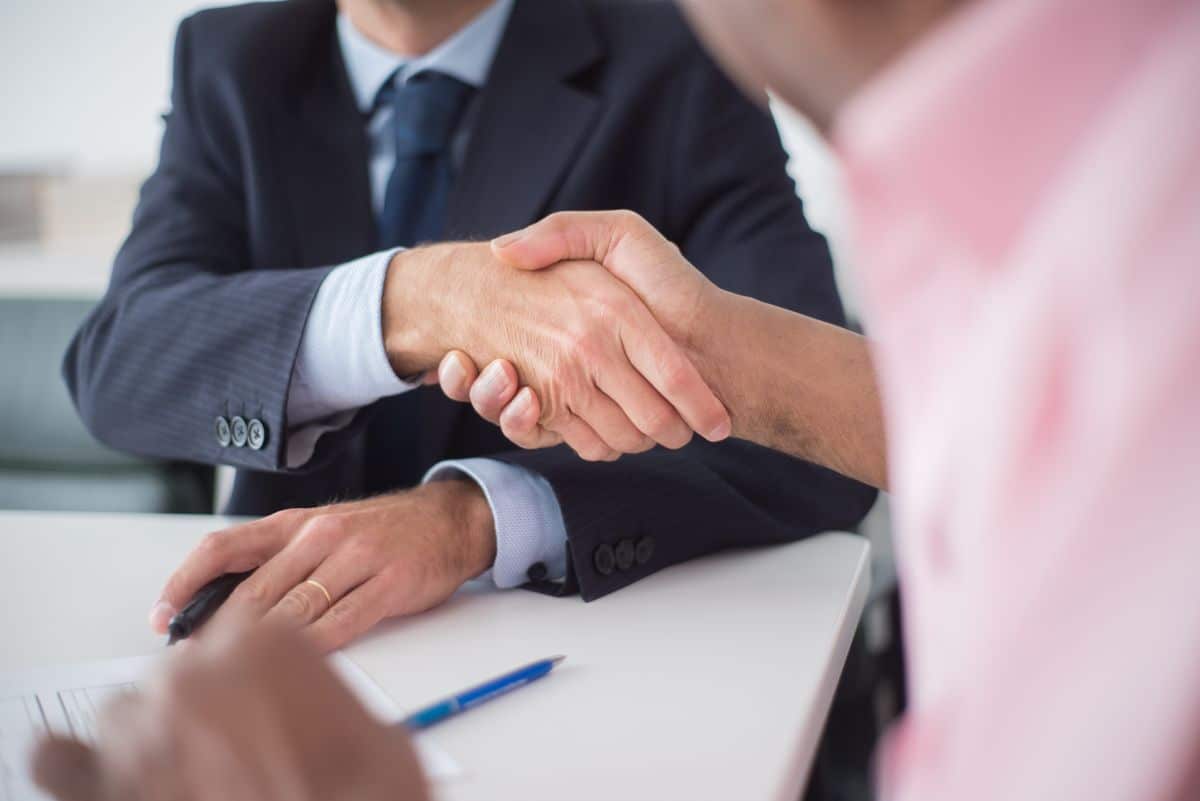 Aperto de maos entre dois executivos sobre a mesa de reuniao, representando acordo corporativo com companhias aereas