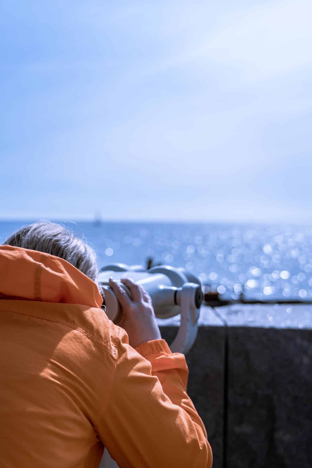 Pessoa observando o mar por um binóculo em mirante, representando a projeção contínua do forecast de viagens corporativas