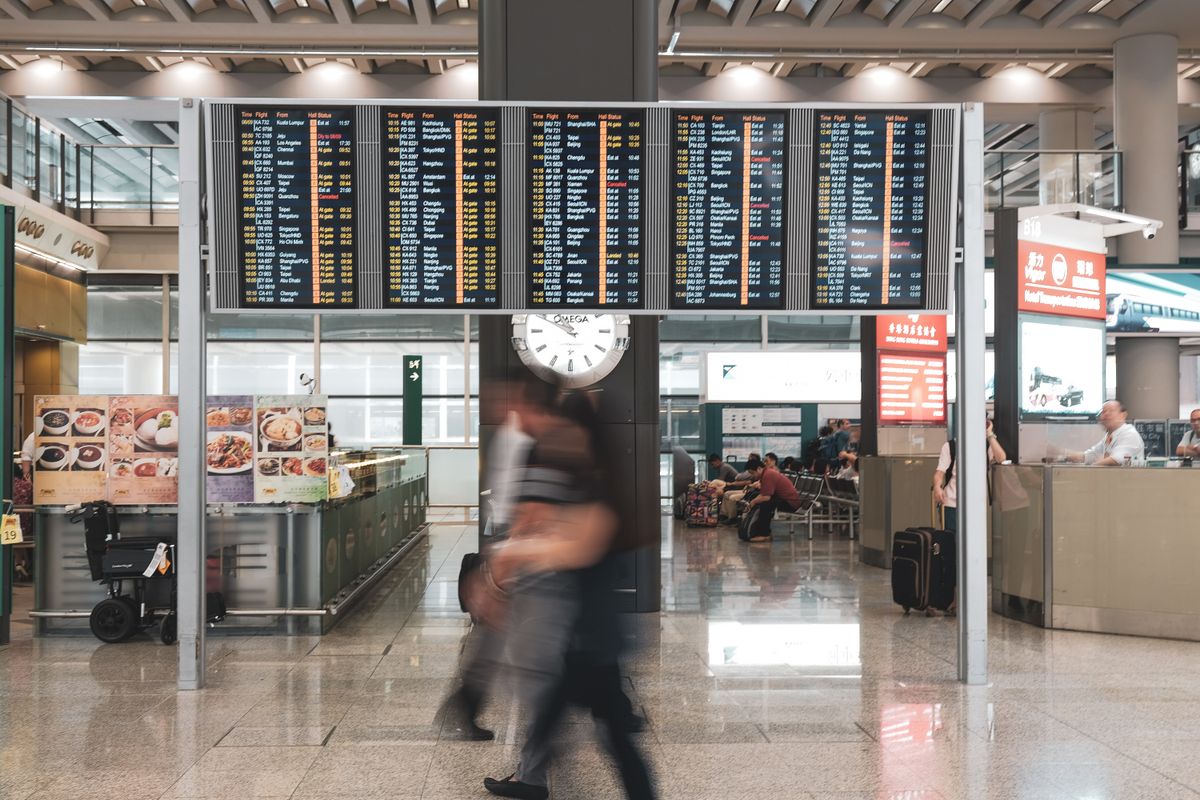 Painel de voos em aeroporto com passageiro em movimento, representando plano de contingencia de viagens