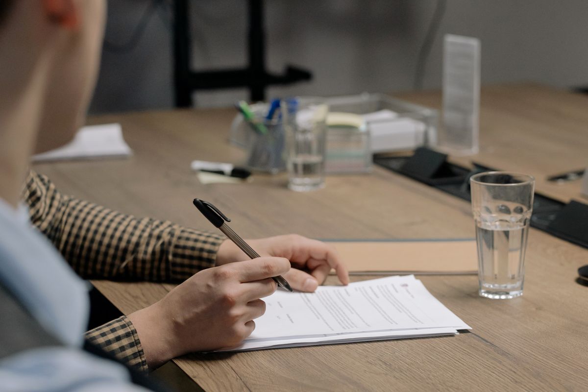 Pessoa assinando documento em mesa de reuniao, representando contrato de terceiros e PJ em viagens