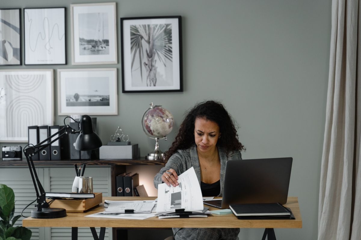 Mulher analisando relatórios impressos na mesa de trabalho, ao lado do notebook, representando a provisão de despesas de viagem no fechamento contábil