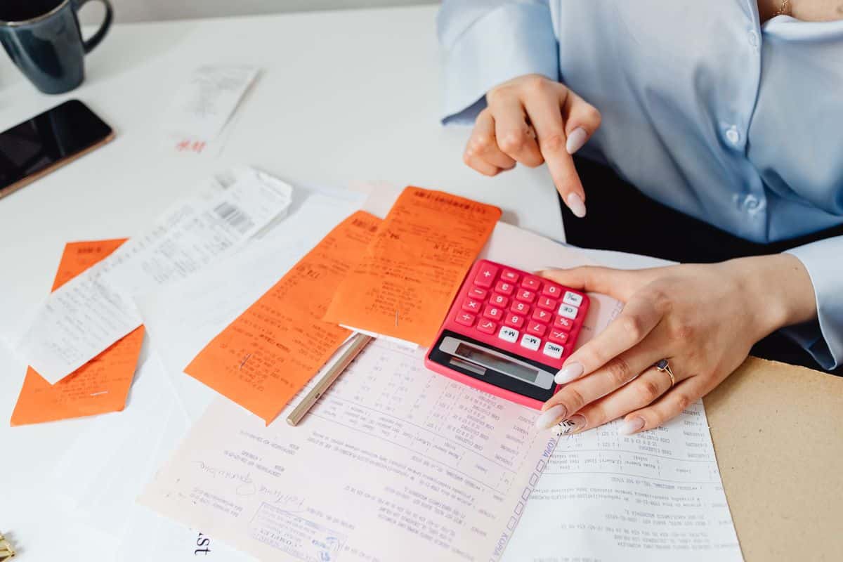 Profissional com calculadora e comprovantes de despesa sobre a mesa, representando o rateio de despesas de viagem
