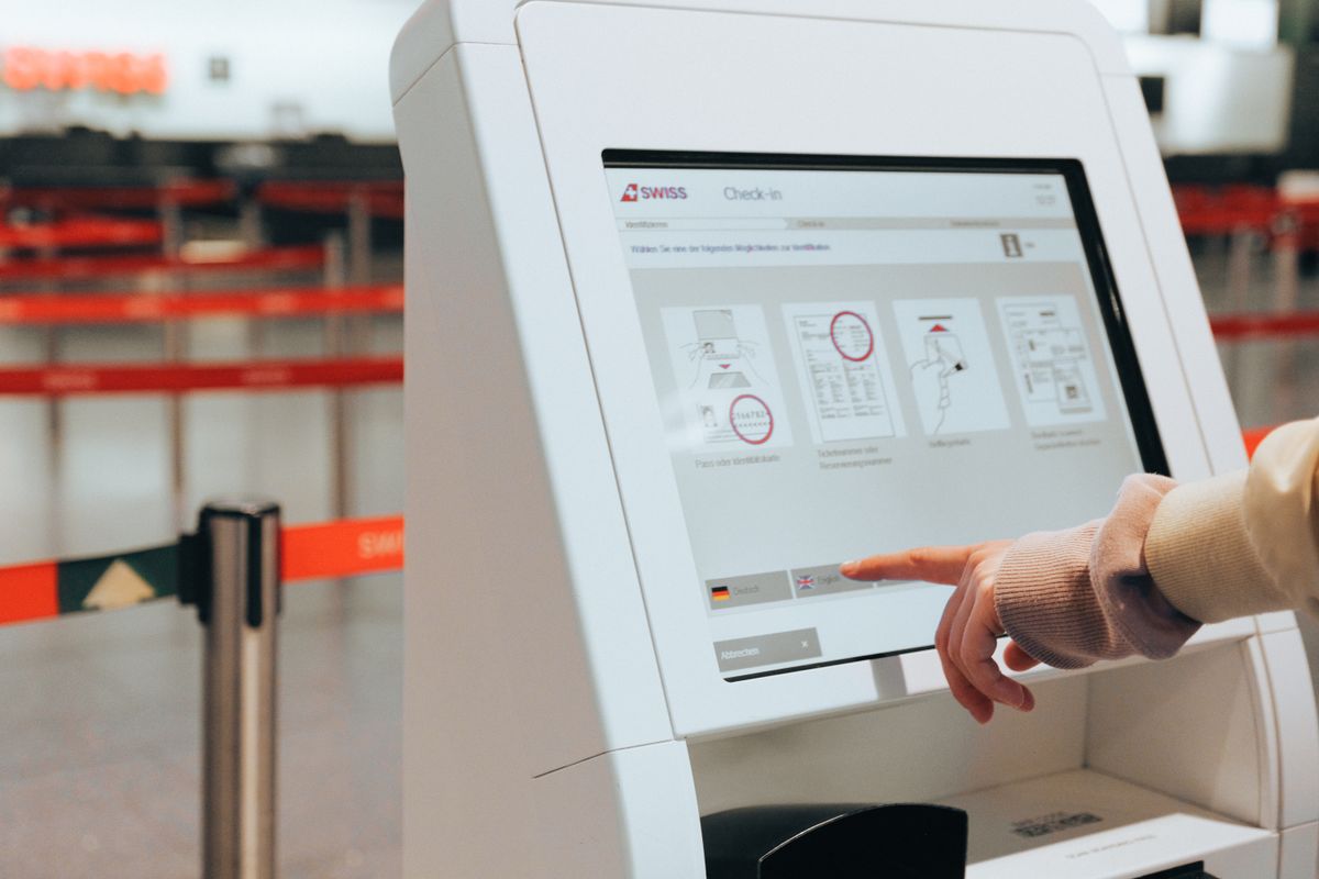 Passageiro usando totem de autoatendimento de check-in em aeroporto, representando a escolha da tarifa aerea