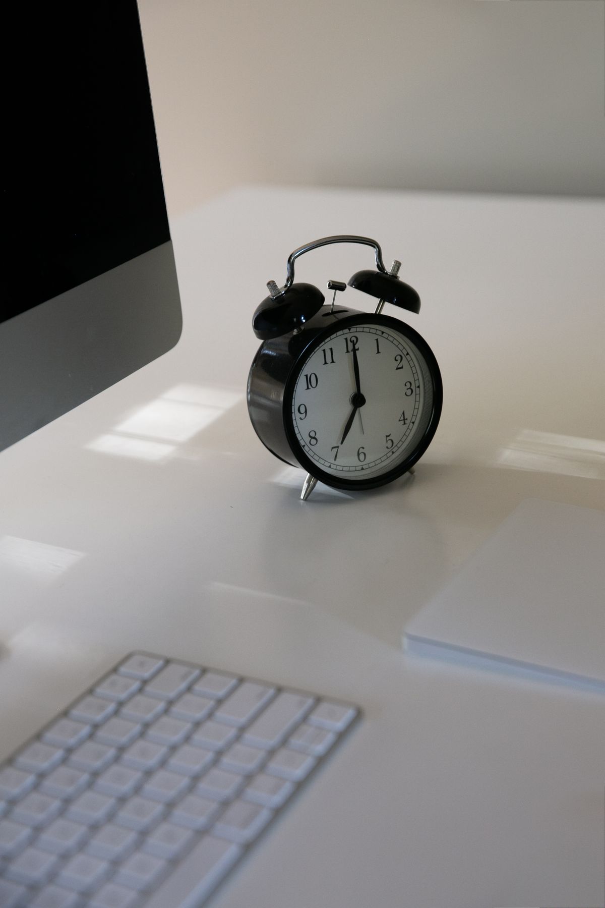 Despertador sobre mesa de escritorio ao lado de monitor e teclado, representando o custo do tempo em viagem